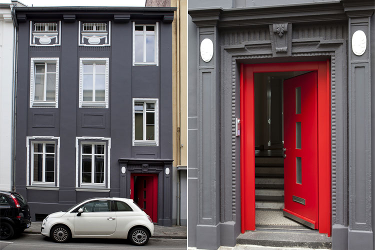 Hausfassade grau mit weiß abgesetzten Fenstern und roter Eingangstüre in Neuss