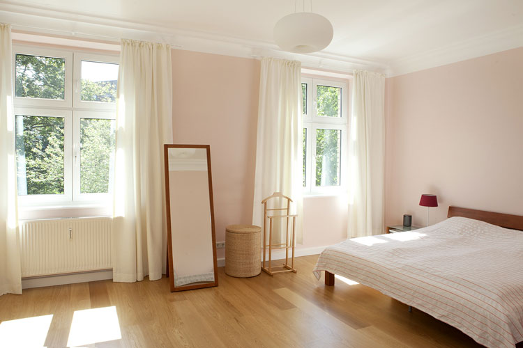 Wohnungsmodernisierung Schlafzimmer mit Holzdielenboden Doppelbett und raumhohen Gardinen und Deckenleuchte in Düsseldorf-Zooviertel